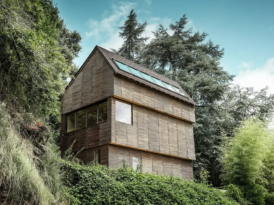 Ein Haus im Westen Frankreichs mit PREFA-Dachschindeln in der Farbe P.10 Walnussbraun, gelegen an einem steilen Hang – ein modernes Design mit einer Fassade aus Weidenholz und einem energieeffizienten Dach.