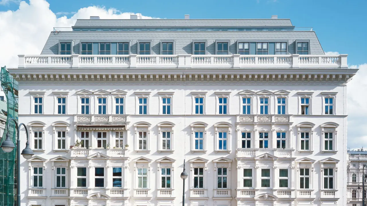 Ausgebautes Dachgeschoss des berühmten Hotel Sacher in Wien mit hellgrauer Mansarddachdeckung, gleichmäßig angeordneten Dachgauben und integrierten Dachflächenfenstern, harmonisch in die klassizistische Fassadenarchitektur eingebunden.