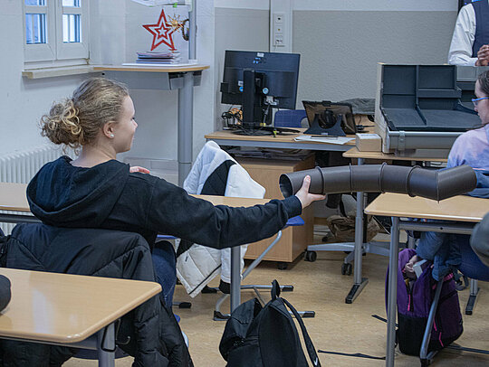 Während der Präsentation von Klempnermeister Marvin Bürger und Dachdeckermeisterin Fabienne Ellermeier wird ein Stück Aluminiumrohr durch die Klasse gereicht. Die Schüler hören aufmerksam zu, während das Gesellenstück vorgestellt wird. 