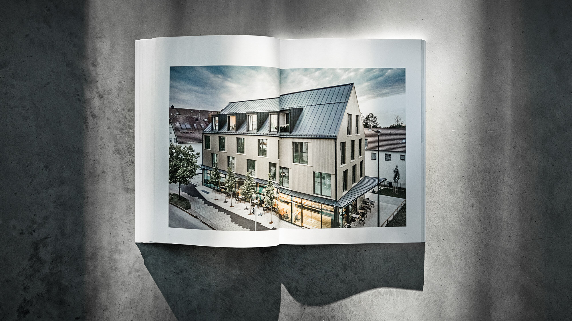 Das geöffnete PREFARENZEN Buch 2024 mit einer Doppelseite, auf der das Wohn- und Geschäftshaus Feldkirchen vom Architekturbüro Heigl abgebildet ist, vor einem grauen Hintergrund.