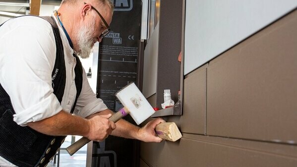Auf dem Bild sieht man den PREFA-Anwendungstechniker Tom Weiß, der ein Stück Siding-Fassade auswechselt. Er ist gerade dabei, das neue Fassadenteil präzise in die bestehende Struktur einzupassen.