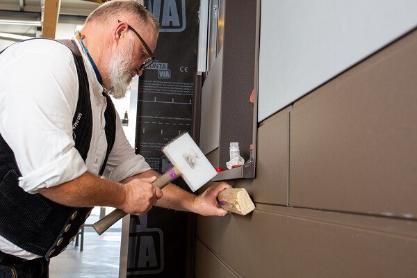 Auf dem Bild sieht man den PREFA-Anwendungstechniker Tom Weiß, der ein Stück Siding-Fassade auswechselt. Er ist gerade dabei, das neue Fassadenteil präzise in die bestehende Struktur einzupassen.