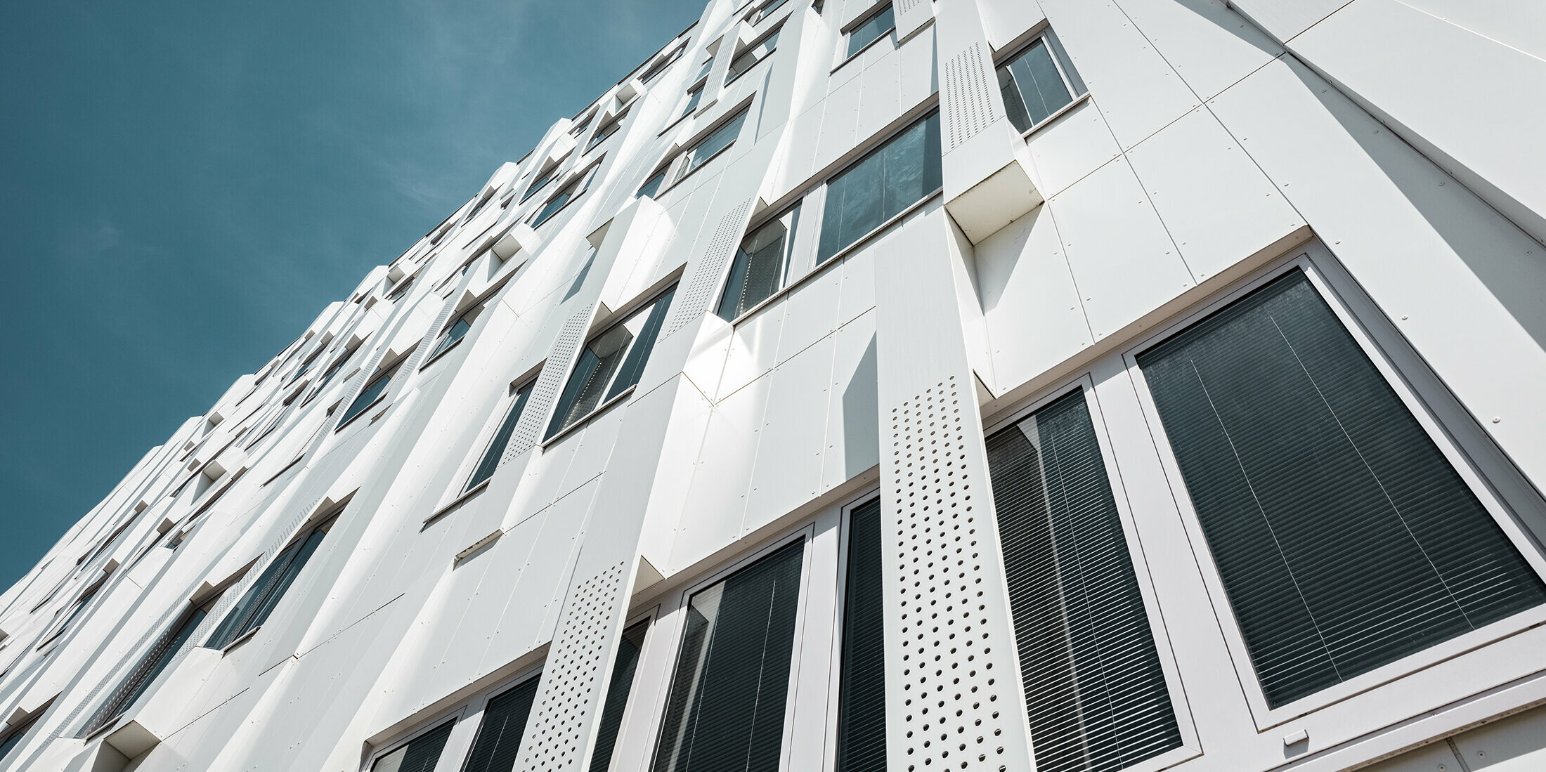 Nahaufnahme der 3D-Fassade mit gelochten Aluminium Verbundplatten-Kassetten und normalen PREFA Verbundplatten in Reinweiß. Die Kassettenfassade von PREFA macht das Gebäude zu einem Blickfang.