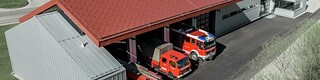 Feuerwehrautos im Feuerwehrhaus der Betriebsfeuerwehr der Firma PREFA. Das Gebäude hat ein rotes Rautendach aus nicht brennbarem Aluminium und eine Alufassade.
