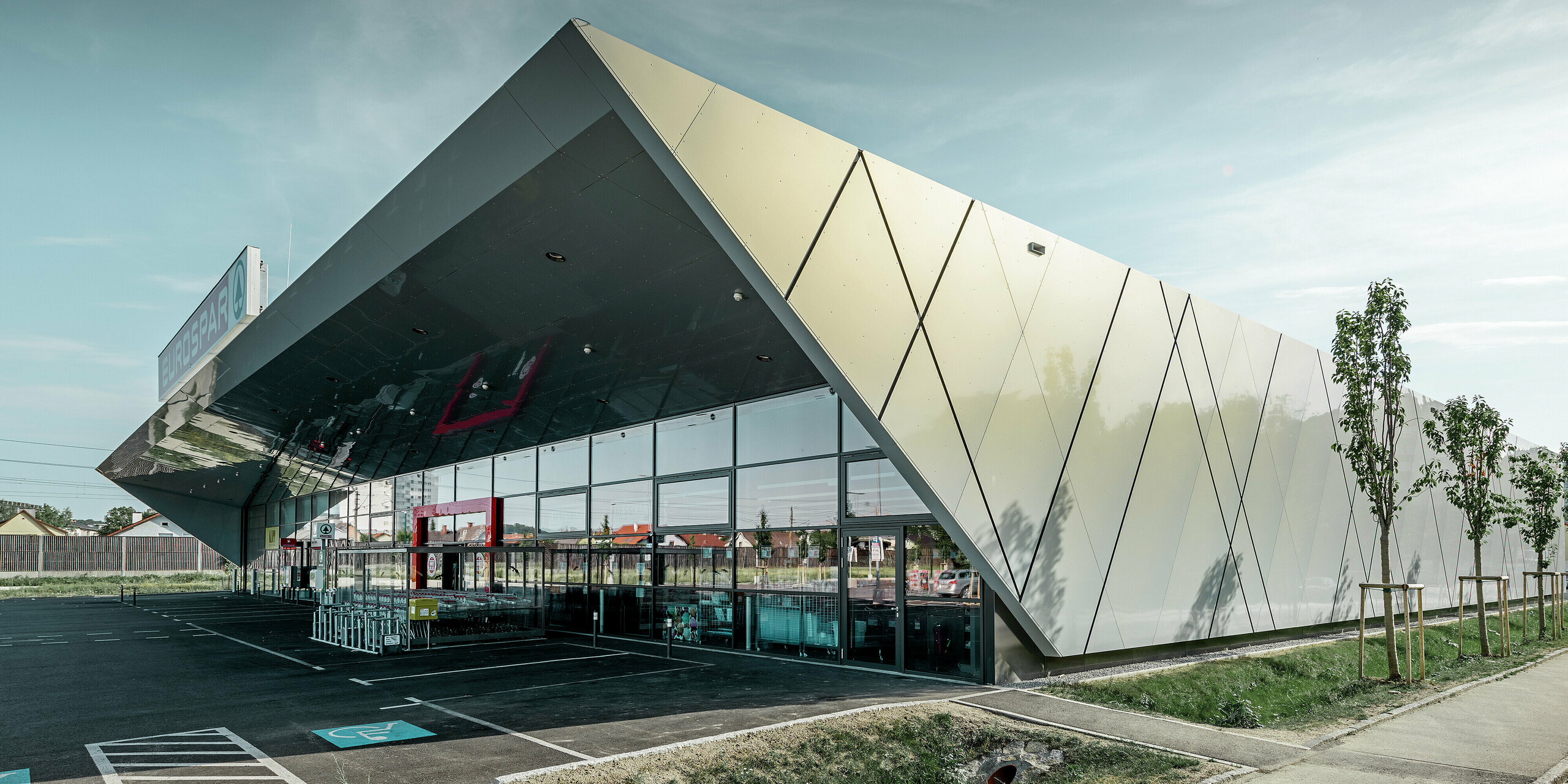 Der Eingangsbereich des EUROSPAR Supermarkts kombiniert großzügige Glasflächen mit einer markanten PREFA Aluminiumfassade. Die glänzende Oberfläche der Sonderfarbe Silver Gold unterstreicht die hochwertige, zukunftsorientierte Architektur der Supermarktfiliale. Die Aluminium Verbundplatten schillern in der Sonne je nach Blickwinkel in unterschiedlichen Farben.