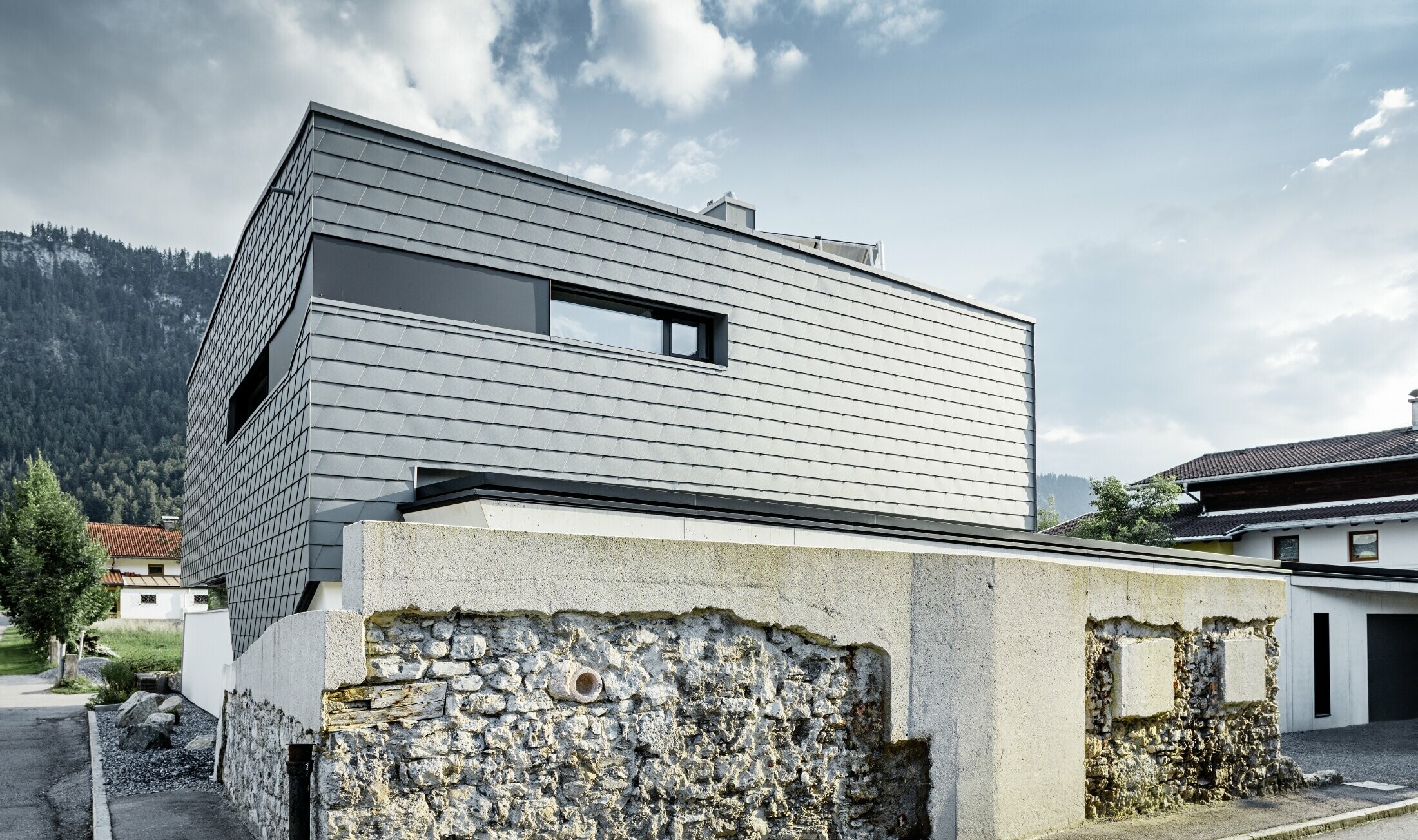 modernes Einfamilienhaus mit Flachdach, großen Fensterflächen und einer Schindel-Fassade in hellgrau aus Aluminium von PREFA
