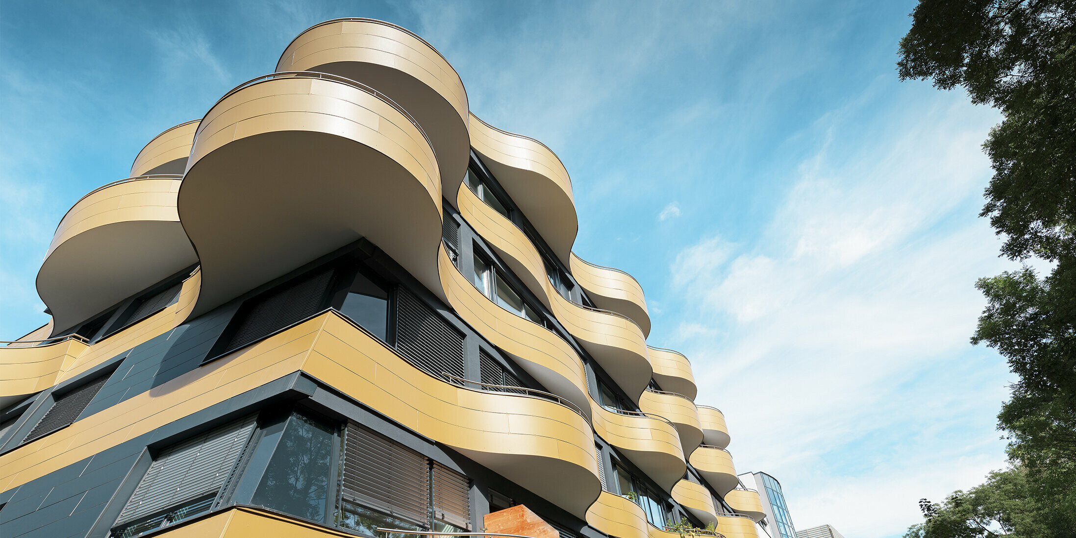Froschperspektive auf die Gebäudeecke der Wohnhausanlage "Goldene Welle" in Graz. Das Gebäude ist mit einzigartigen Rundbalkonen ausgestattet, die mit robusten Aluminiumverbundplatten verkleidet sind.