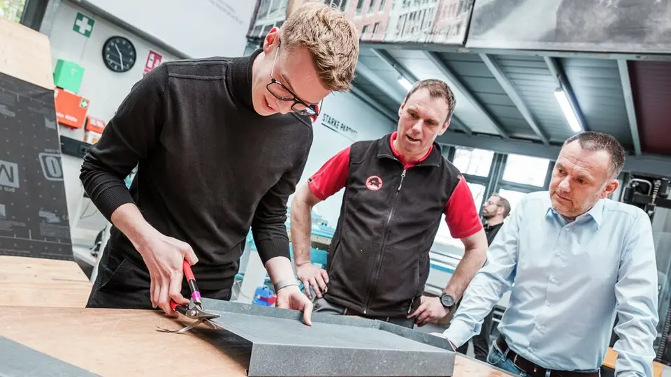 Praxisnahe Schulung in unserer Academy in Hamburg: Ein Teilnehmer bearbeitet unter Anleitung eines PREFA-Lehrverlegers ein Metallblech mit einer Blechschere.