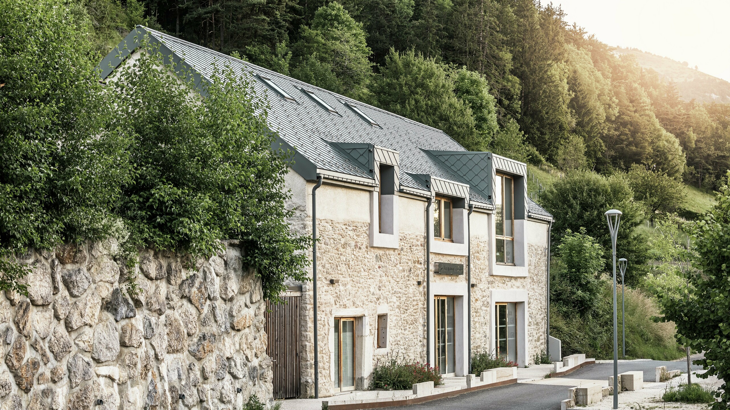 Die restaurierte Scheune "La Grange à Gaby" in Engins, Frankreich. Das Gebäude kombiniert traditionelles Steinemauerwerk mit einem modernen PREFA Aluminiumdach aus 29 × 29 cm großen Rauten. Die Sanierung verbindet historische Bauweise mit zeitgemäßer Architektur und nachhaltigen Materialien.
