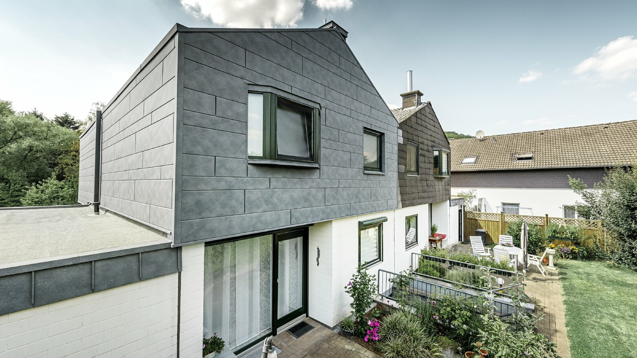 Der obere Gebäudeteil der Doppelhaushälfte wurde mit dem PREFA Fassadenelement Siding.X in P.10 Steingrau saniert. Gleich daneben zum Vergleich die Haushälfte vor der Sanierung.