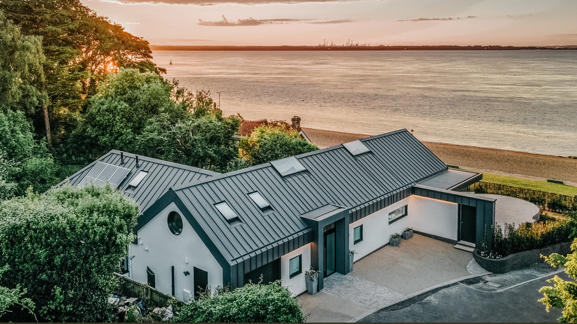 Der Bungalow von der Straßenseite aus der seitlichen Vogelperspektive, der Strand und das Meer breiten sich davor aus. 