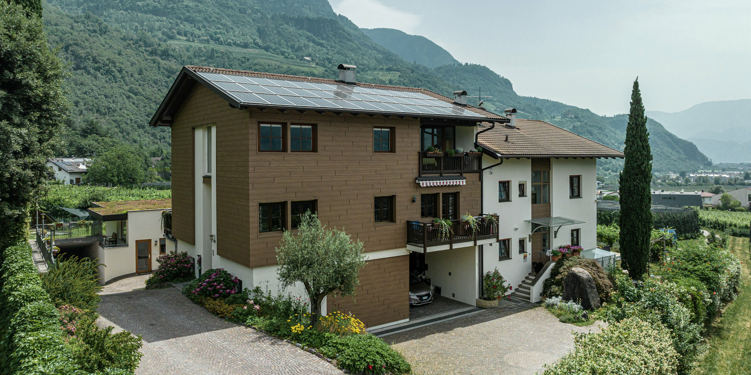 Sanierte Ferienwohnungen Prechtlhof in Meran, Südtirol, mit PREFA Sidings in Walnussbraun und einer Photovoltaikanlage am Dach. Die langlebige Aluminiumfassade in Holzoptik sorgt für natürliche Ästhetik, höchste Widerstandsfähigkeit und geringen Wartungsaufwand, ideal für die alpine Umgebung.