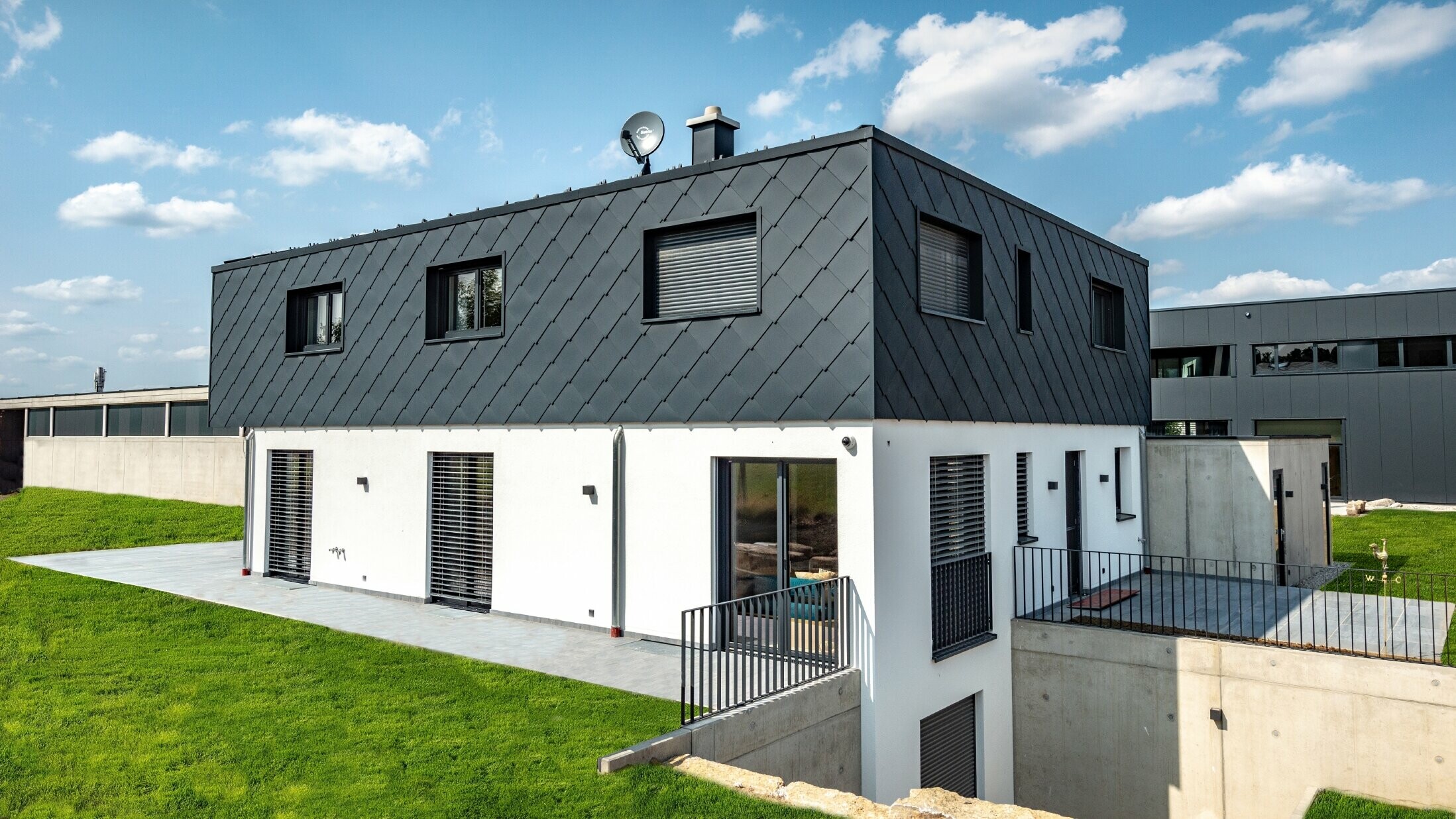 Schlichter Neubau mit Flachdach, das Erdgeschoß ist weiß verputzt, das Obergeschoß ist mit der großen PREFA Wandraute in Anthrazit verkleidet.