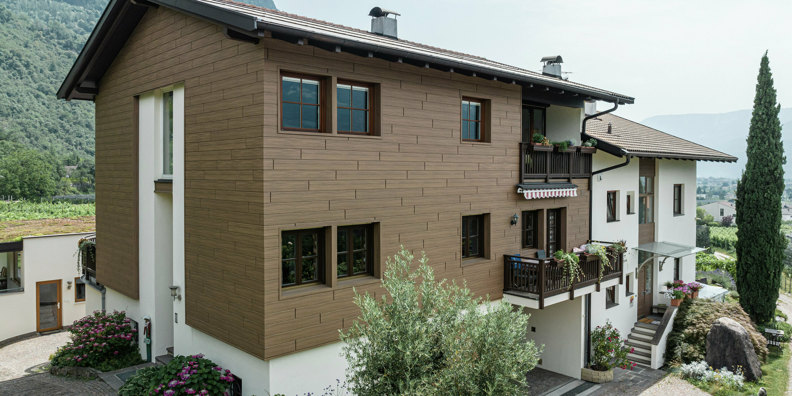 Die modernisierten Ferienwohnungen Prechtlhof in Meran, Südtirol, mit einer langlebigen PREFA Fassade in Walnussbraun. Die Aluminium-Sidings in Holzoptik verbinden traditionelle Ästhetik mit wartungsfreier Langlebigkeit und fügen sich harmonisch in die alpine Landschaft ein.