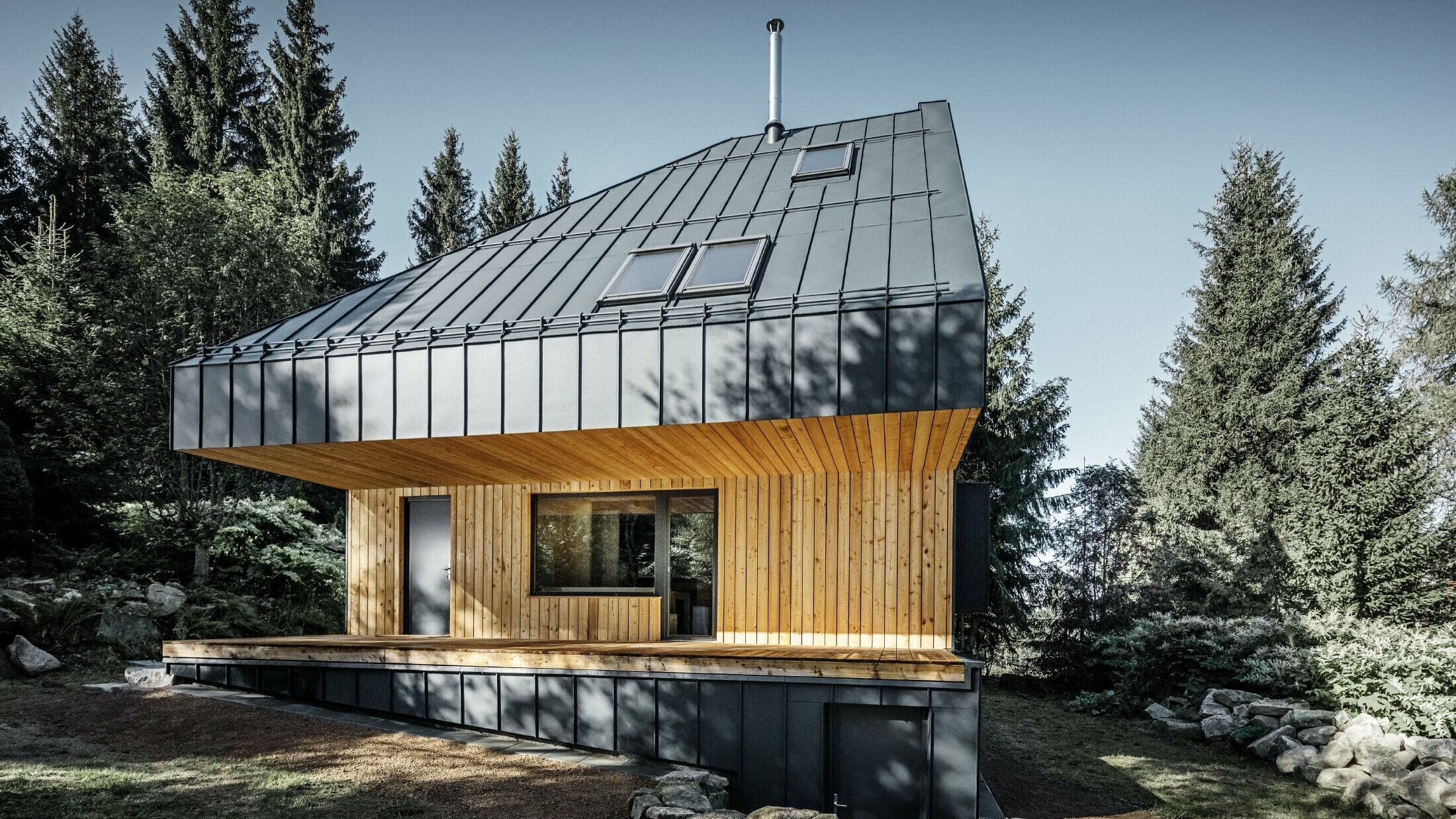 Architektonisches Einfamilienhaus im Wald, das imposante Dach wurde mit Prefalz Aluminium von PREFA in Anthrazit verkleidet. Die Untersicht sowie die Fassade ist mit Holzpaneelen verkleidet.