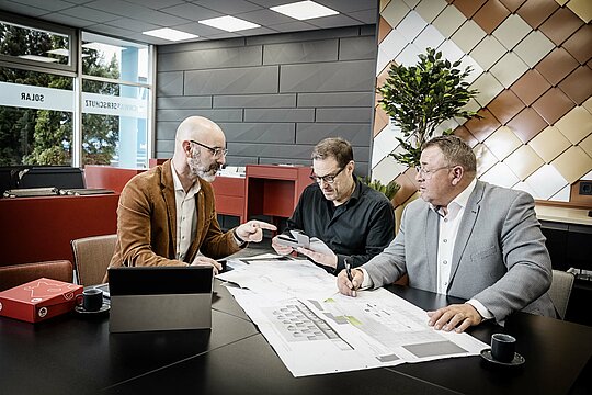 PREFA Vertriebsleiter Frieder Zaiß im Kundengespräch am Besprechungstisch im PREFA Schauraum in München. Die Wände im Hintergrund sind mit verschiedenen PREFA Produkten verkleidet.