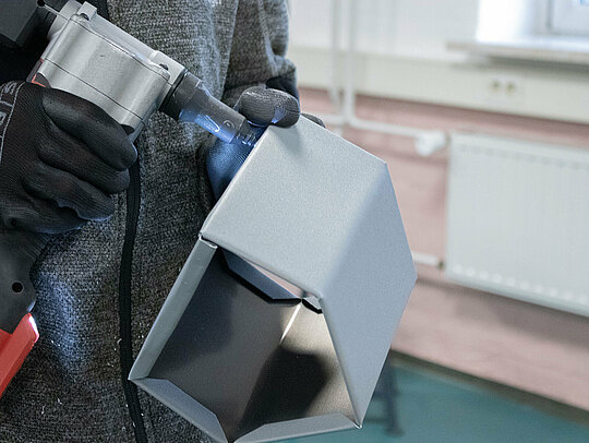 Klempnermeister Marvin Bürger fixiert das Aluminium-Vogelhaus mit einer Nietzange. Er hält das Werkzeug in der Hand und arbeitet sorgfältig an den letzten Verbindungen des Vogelhauses.