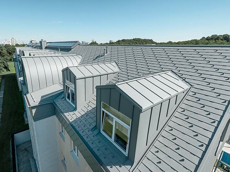 Ausgebauter Dachboden mit Gauben und Fenstern; Das Dach wurde mit der PREFA Dachschindel in Hellgrau und die Gauben mit Prefalz in Hellgrau verkleidet.