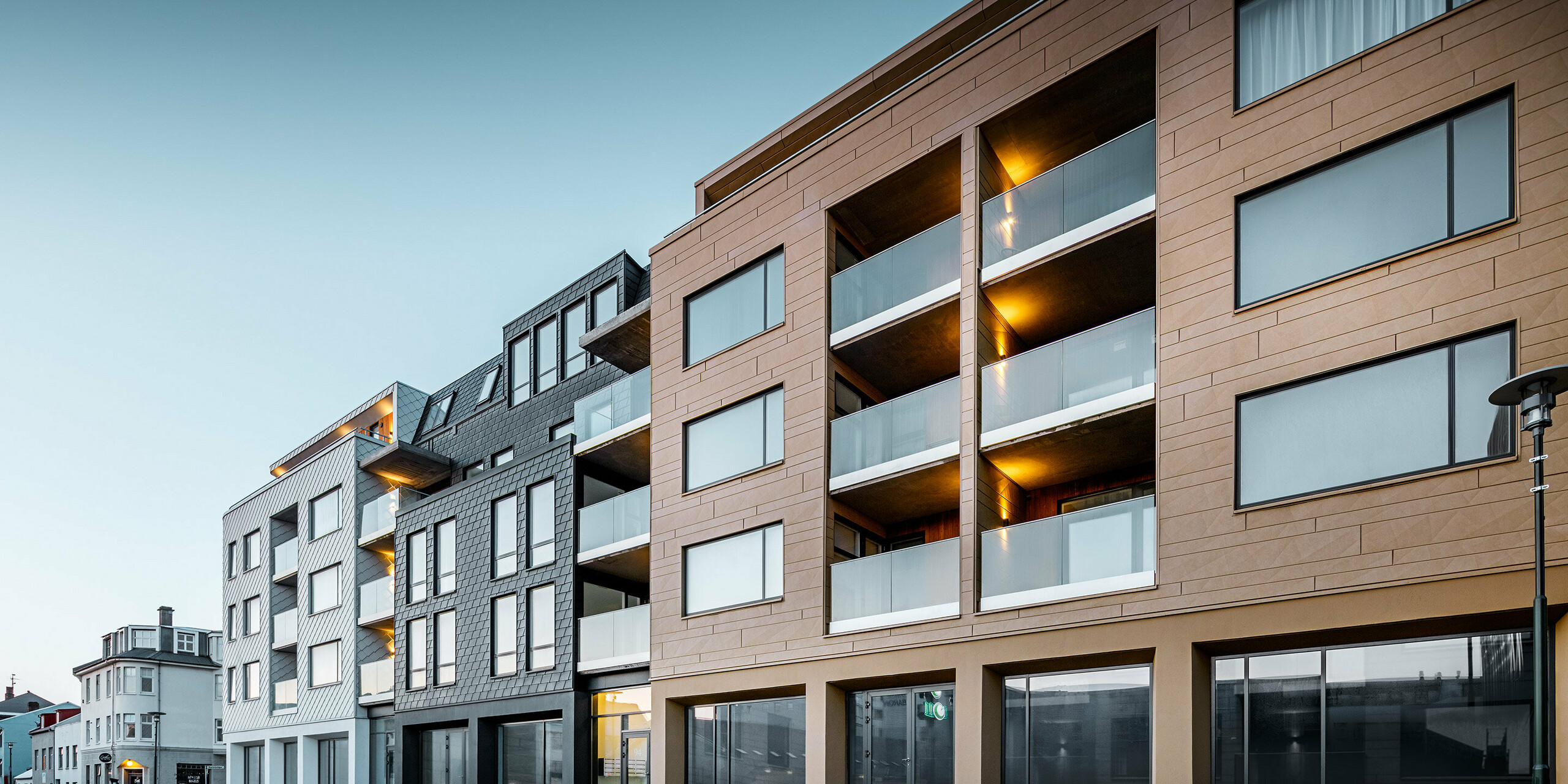 Seitliche Vorderansicht des Gebäudes - verkleidet mit Schindeln, Rauten und Siding.X in den Farben Weiß, Anthrazit und Sandfarben.