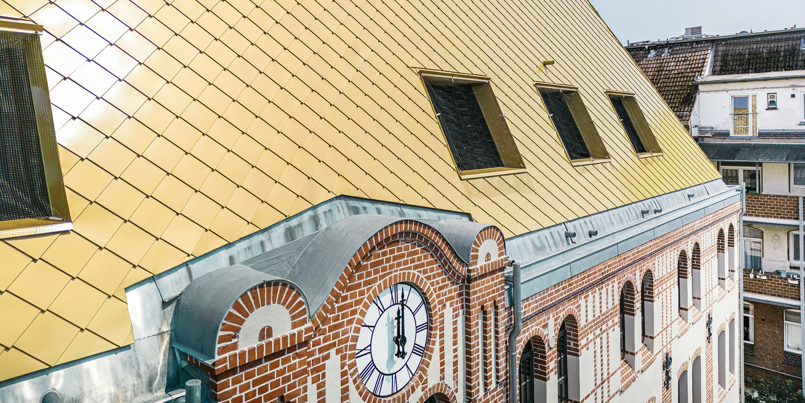 Nahaufnahme der speziellen Dachlandschaft des Studentenwohnheims "The Station" in Kiel. Das Gebäude wurde mit PREFA Dach- und Wandrauten 29 × 29 in der Farbe Mayagold verkleidet.