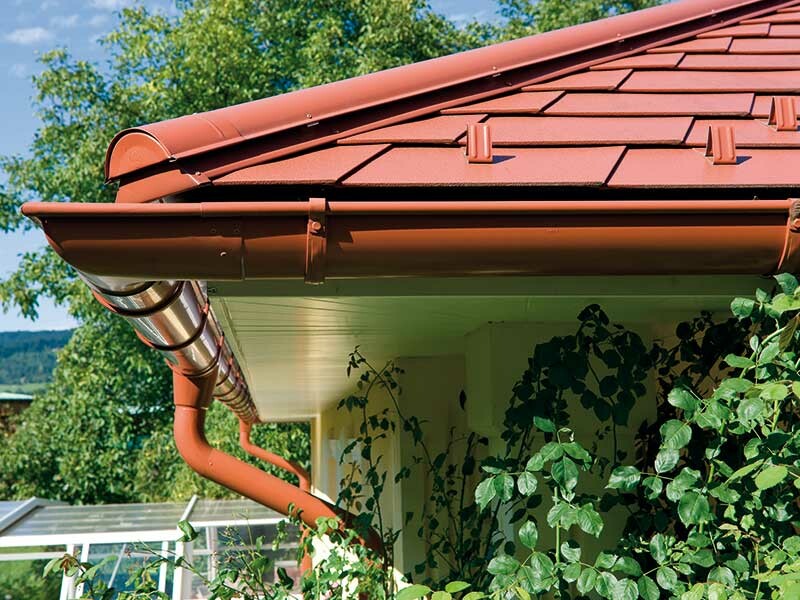 Detailaufnahme der PREFA Dachschindel in Ziegelrot mit der dazu passenden Dachrinne ebenfalls in Ziegelrot.