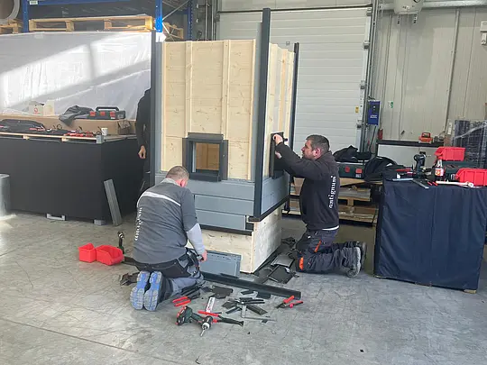 Zwei Fachkräfte arbeiten an der Montage des PREFA Academy Cube Trainingsmoduls in einer Werkhalle und installieren die modulare Konstruktion für praxisnahe Schulungen vor Ort.
