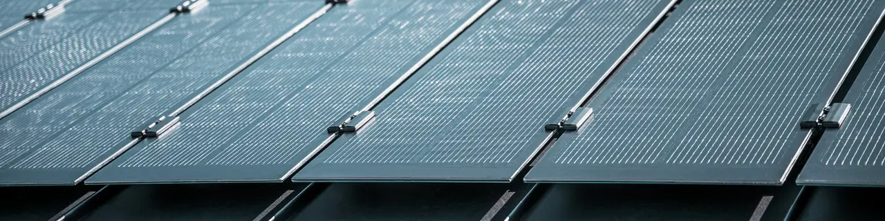 Montageansicht mehrerer PREFALZ Solarmodule auf einem bestehenden PREFALZ Dach in Meschede, Deutschland. Die rahmenlosen Glas/Glas-PV-Module sind in präzisen Reihen angeordnet und mit robusten Halterungen fixiert, was eine flächenbündige, elegante Optik erzeugt. Die hochwertige Befestigungstechnik sorgt für Stabilität und Langlebigkeit, während die innovative TOPCon-Zellentechnologie maximale Energieeffizienz garantiert. Das Bild vermittelt modernste Photovoltaik-Lösung, die Design, Funktionalität und Nachhaltigkeit perfekt vereint.