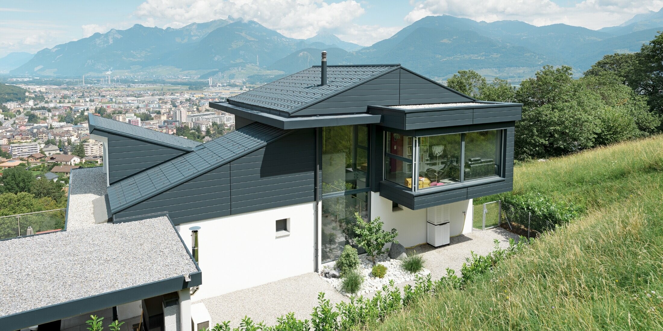 Die Fassade des Einfamilienhauses im Schweizer Ort Choëx ist mit PREFA Sidings in der Farbe P.10 Anthrazit bekleidet. Das Dach wurde mit den bewährten PREFA Dachplatten, ebenfalls in Anthrazit, gedeckt.