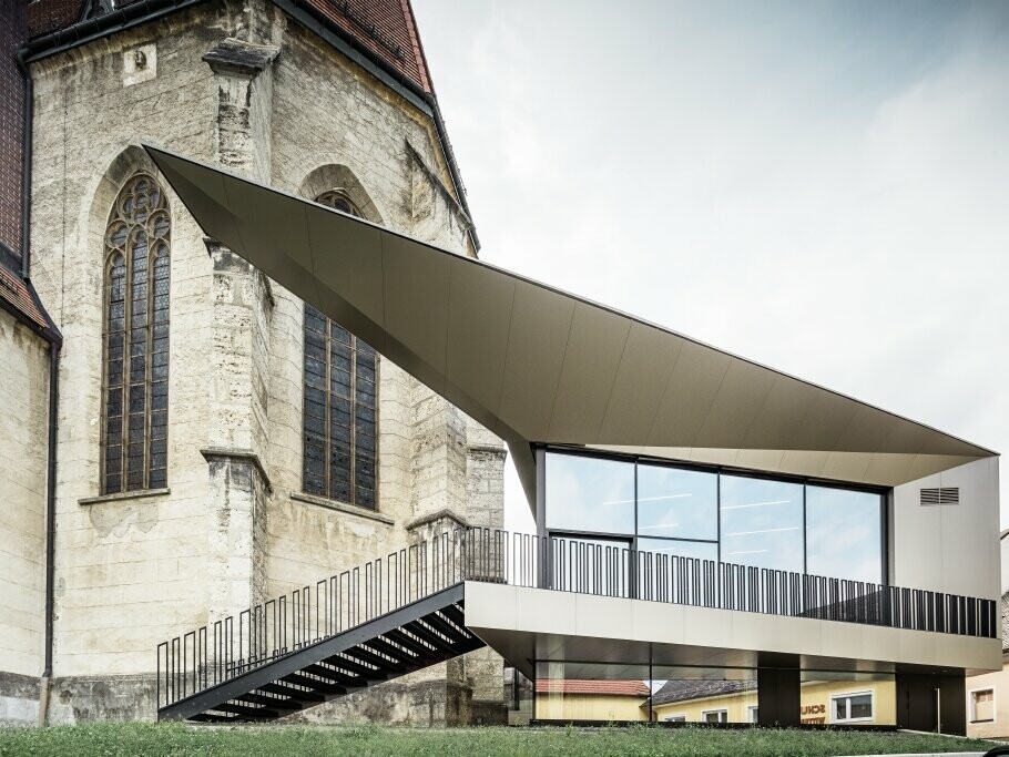 Seitliche Ansicht auf das Pfarrzentrum FOKUS mit PREFA Fassade und die Kirche in Sierning (AT).