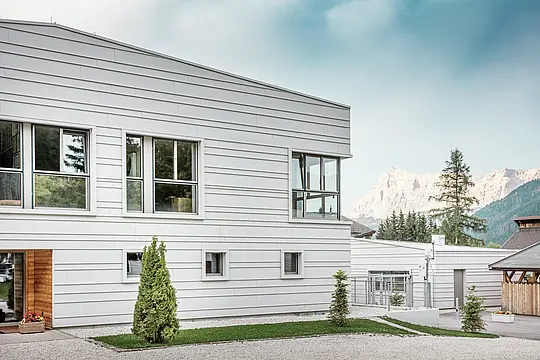 Detailansicht der „Tempesti“-Kaserne mit präzise positionierten PREFALZ-Paneelen in der Farbe P.10 Prefaweiß. Die klaren Linien der horizontal angeordneten, gefalzten Verkleidung unterstreichen das moderne Fassadendesign. Die helle Oberfläche reflektiert das Sonnenlicht und optimiert das Raumklima. Im Hintergrund erhebt sich die imposante Berglandschaft Südtirols – hier trifft Technologie auf Natur in ihrer schönsten Form.