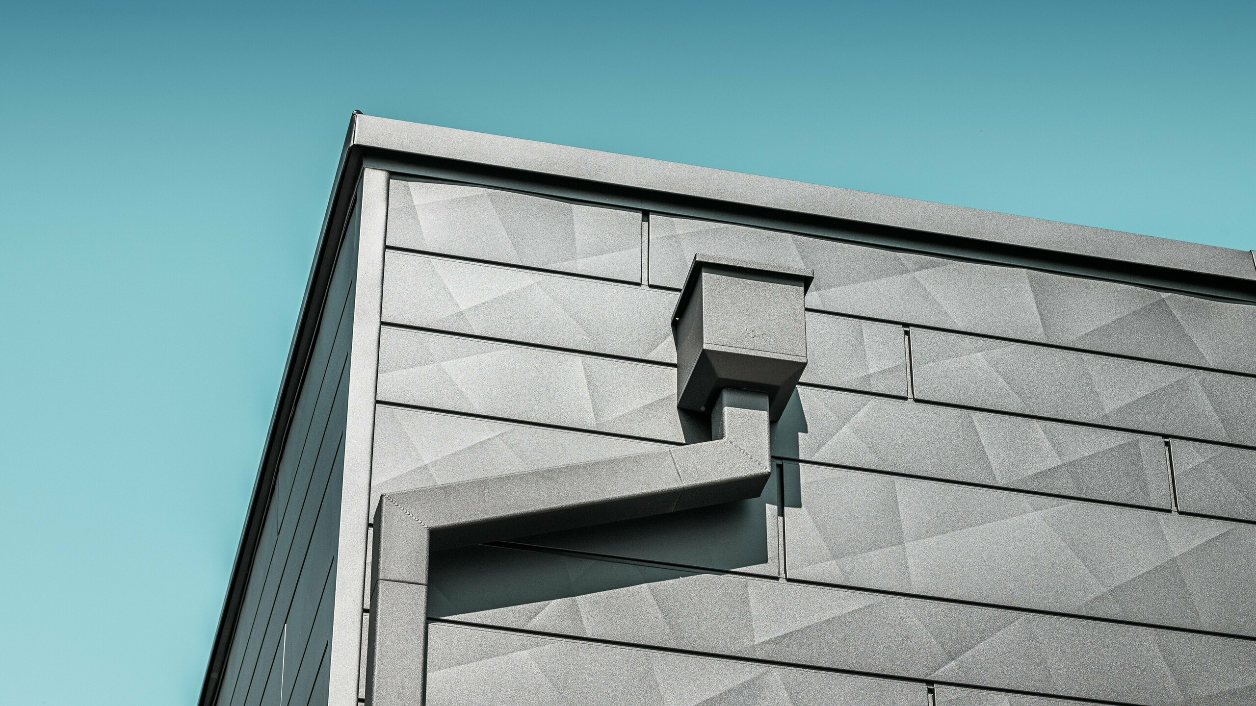 Die Fassade des sanierten Einfamilienhauses in Teuschnitz zieren PREFA Siding.X Aluminiumpaneele in der Farbe P.10 Schwarz mit ihrer einzigartigen, geometrischen Textur. Der Wasserfangkasten und das Quadratrohr von PREFA fügen sich elegant in das Design ein und bieten eine funktionale Lösung für die Entwässerung. Die präzise Verarbeitung und die harmonische Integration der Elemente unterstreichen die ästhetische Qualität und Langlebigkeit der PREFA Aluminiumprodukte.