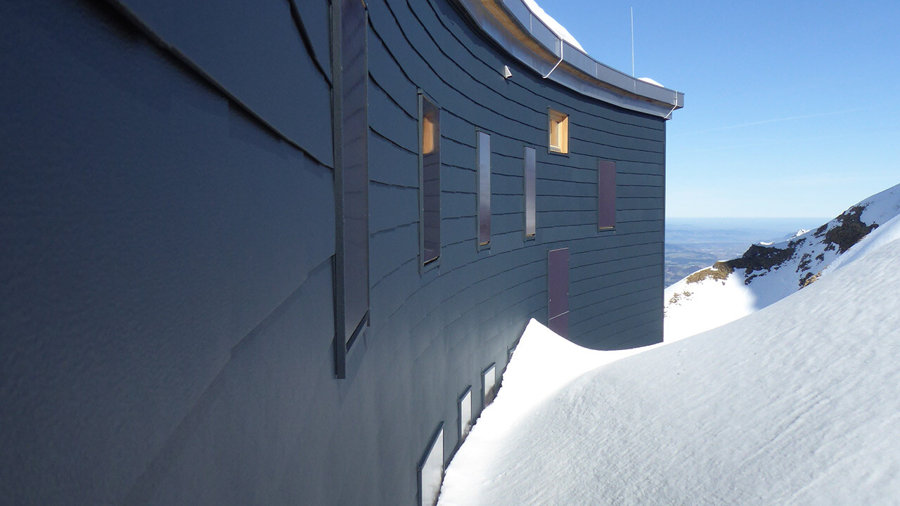 Wandverkleidung der Rückseite des Waltenberger Hauses in den Allgäuer Alpen; Die Fassade ist mit Alu-Schindeln in Anthrazit verkleidet, ein Teil der Fassade wird Schnee verdeckt.