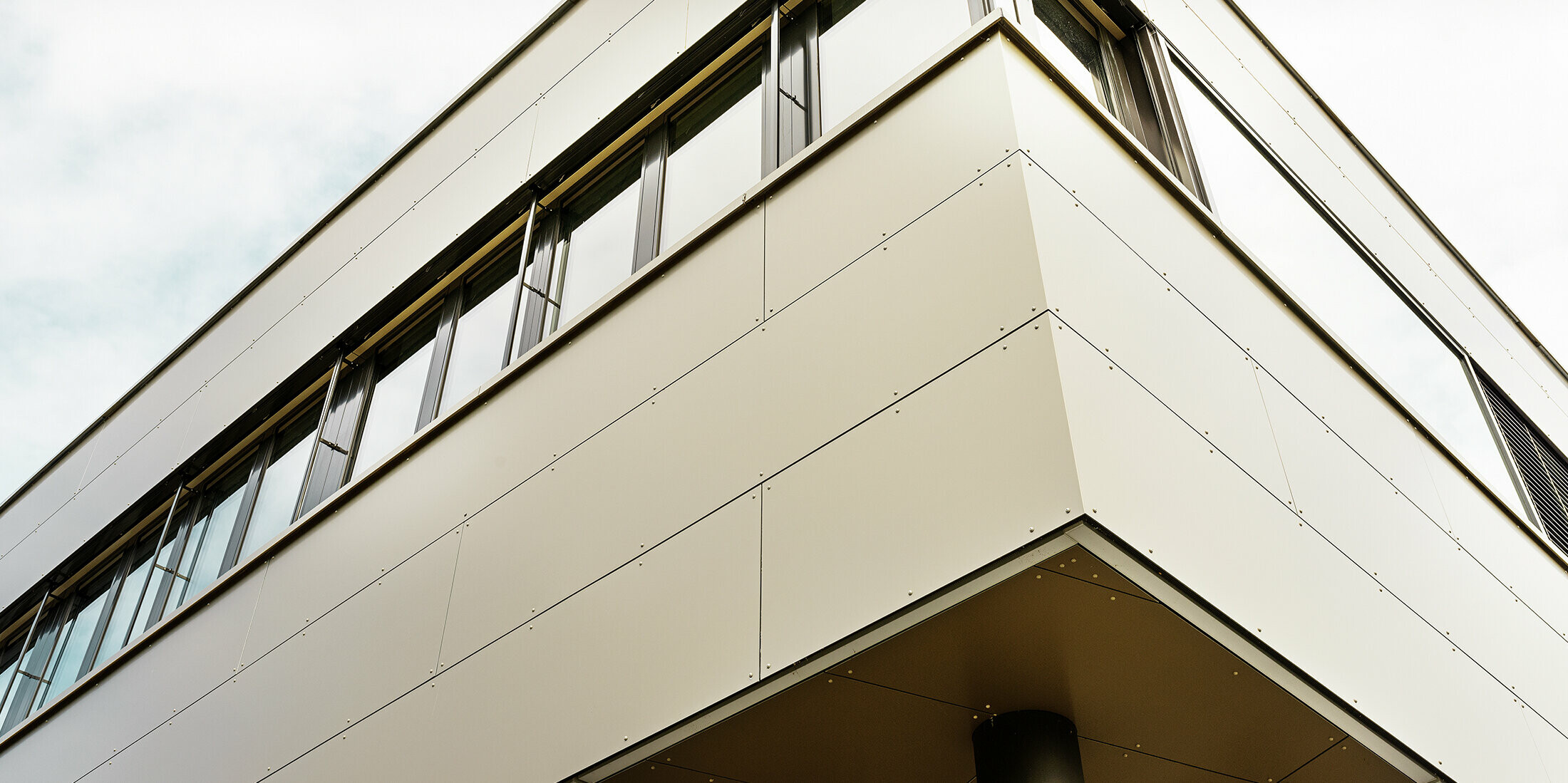 Die Eckaufnahme des Firmengebäudes in Wabern hebt die präzise montierten PREFA Aluminium Verbundplatten in Bronze hervor. Die elegante Flachdacharchitektur und die klar strukturierten Fensterflächen schaffen ein modernes, hochwertiges Erscheinungsbild.