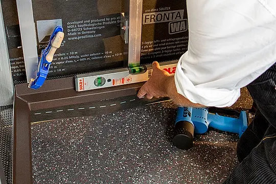 Zu sehen ist das fertig gestaltete Sockelprofil in Braun, welches an die PREFA Fassaden-Unterkonstruktion mithilfe einer Wasserwaage ausgerichtet und anschließend fixiert wird.