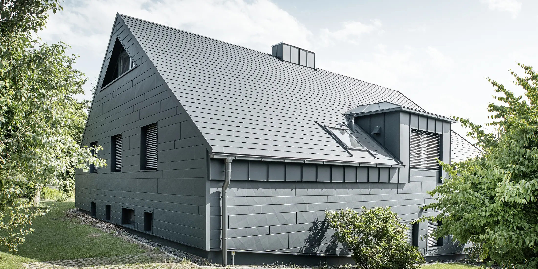 Großes Einfamilienhaus mit Satteldach und vielen Fenstern. Das gesamte Haus wurde mit einer Aluminiumhülle in Anthrazit verkleidet, am Dach kamen PREFA Alu-Dachschindeln zum Einsatz und an der Fassade Siding.X in Anthrazit.