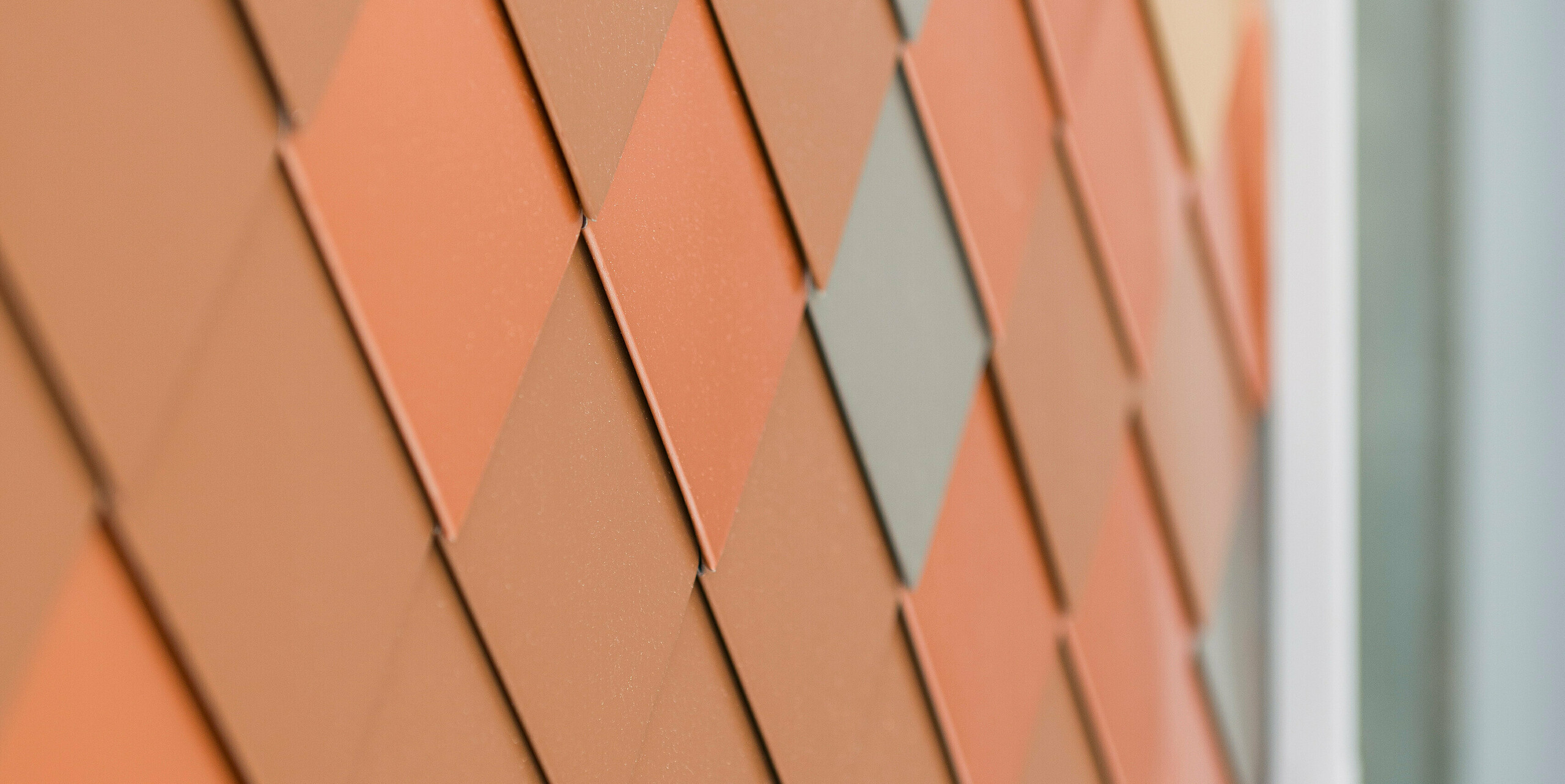 Detailansicht einer modernen Aluminiumfassade von PREFA mit einem geometrischen Muster in verschiedenen Farbtönen. Die kleinen Aluminiumteile aus FALZONAL sind diamantförmig angeordnet und erzeugen eine dreidimensionale Optik, die Struktur und Farbtiefe betont