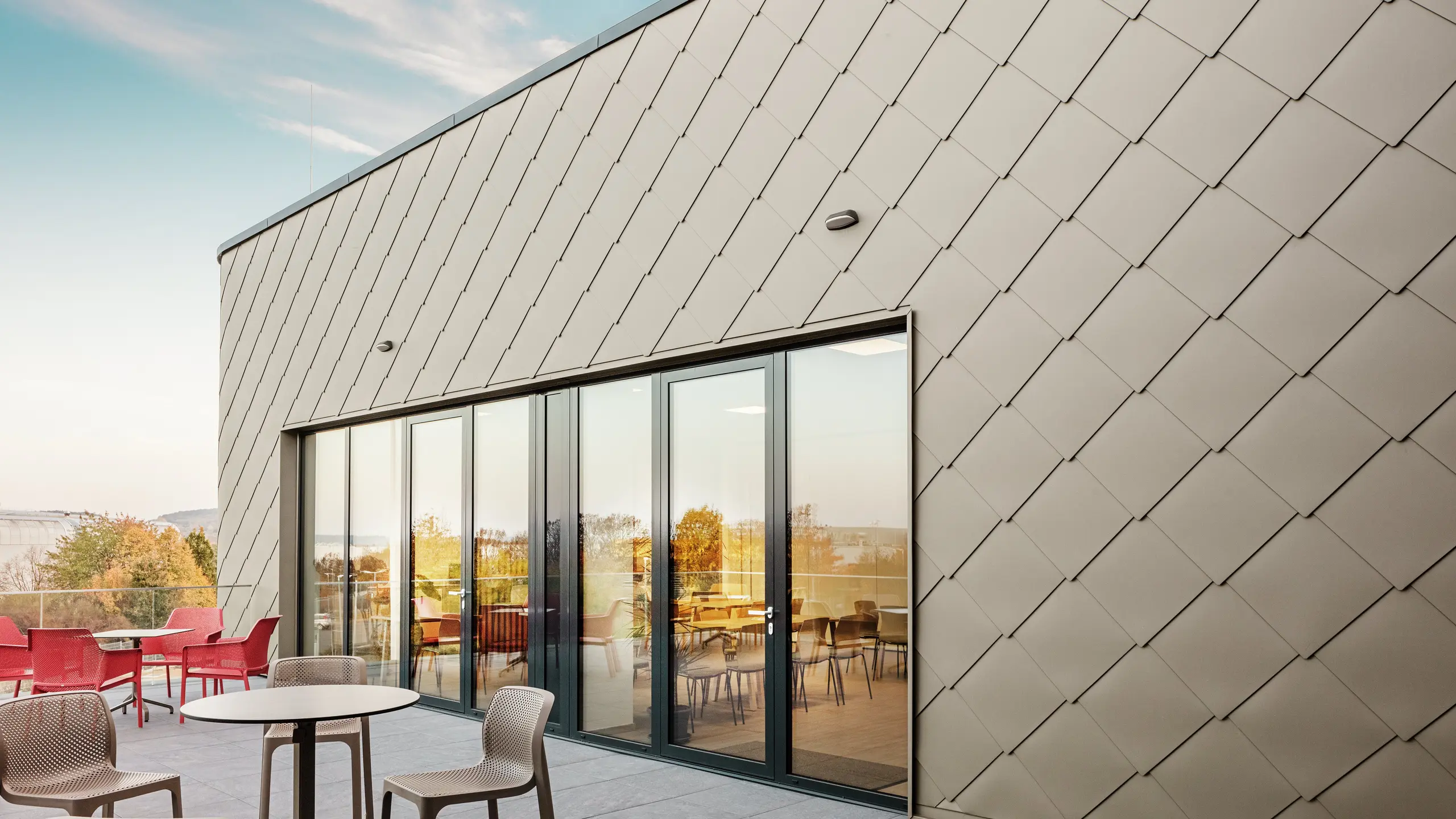 Die Fassade des neuen PREFA Standortes in Törökbálint besticht durch die eleganten PREFA Wandrauten 44 × 44 in P.10 Prefabronze. Die präzise verlegte Aluminiumfassade sorgt für ein modernes, dynamisches Erscheinungsbild und bietet gleichzeitig maximalen Schutz vor Witterungseinflüssen. Die großzügige Glasfront verbindet Innen- und Außenbereich und schafft auf der großzügigen Terrasse eine helle und einladende Atmosphäre.