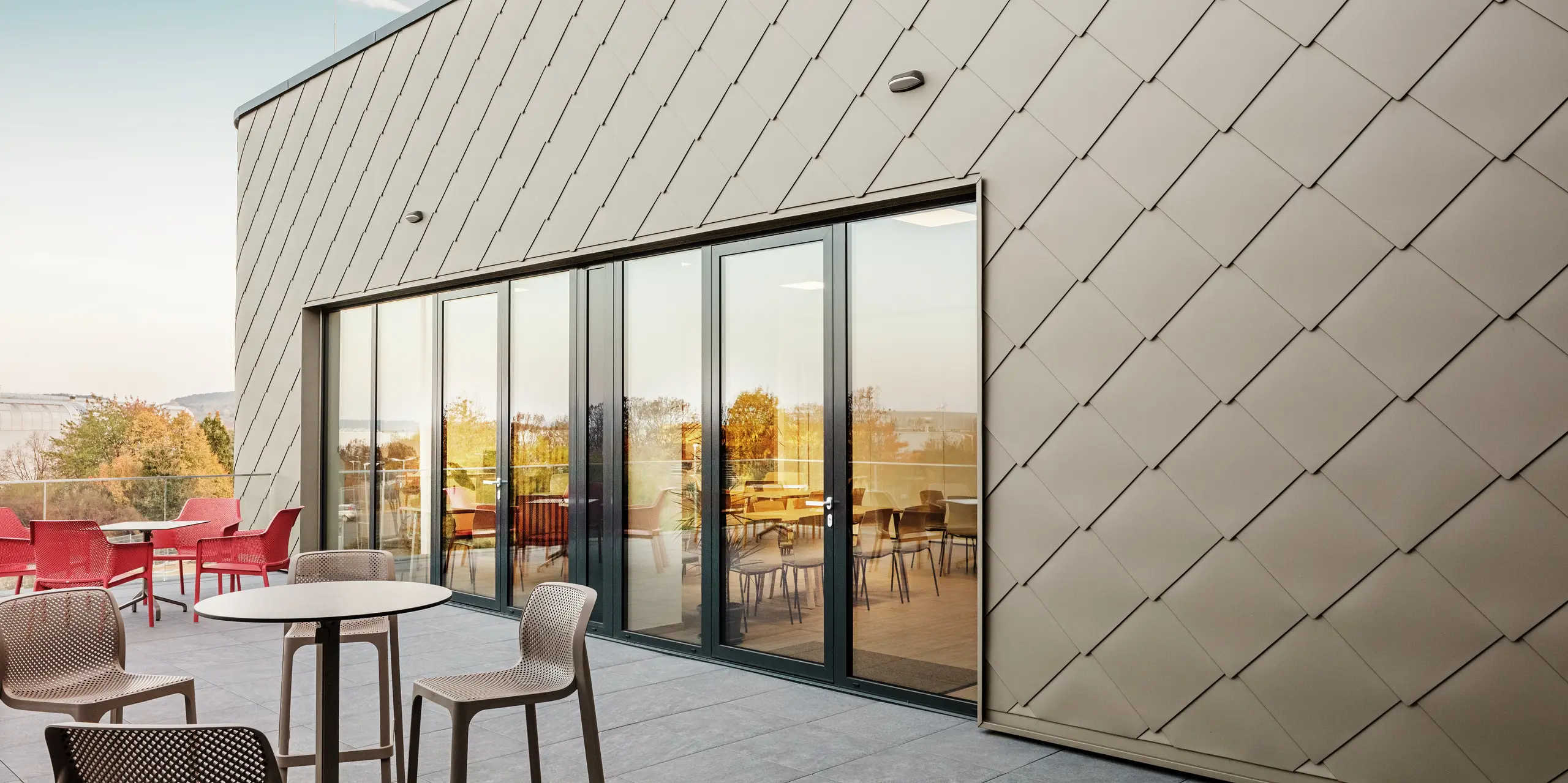 Die Fassade des neuen PREFA Standortes in Törökbálint besticht durch die eleganten PREFA Wandrauten 44 × 44 in P.10 Prefabronze. Die präzise verlegte Aluminiumfassade sorgt für ein modernes, dynamisches Erscheinungsbild und bietet gleichzeitig maximalen Schutz vor Witterungseinflüssen. Die großzügige Glasfront verbindet Innen- und Außenbereich und schafft auf der großzügigen Terrasse eine helle und einladende Atmosphäre.