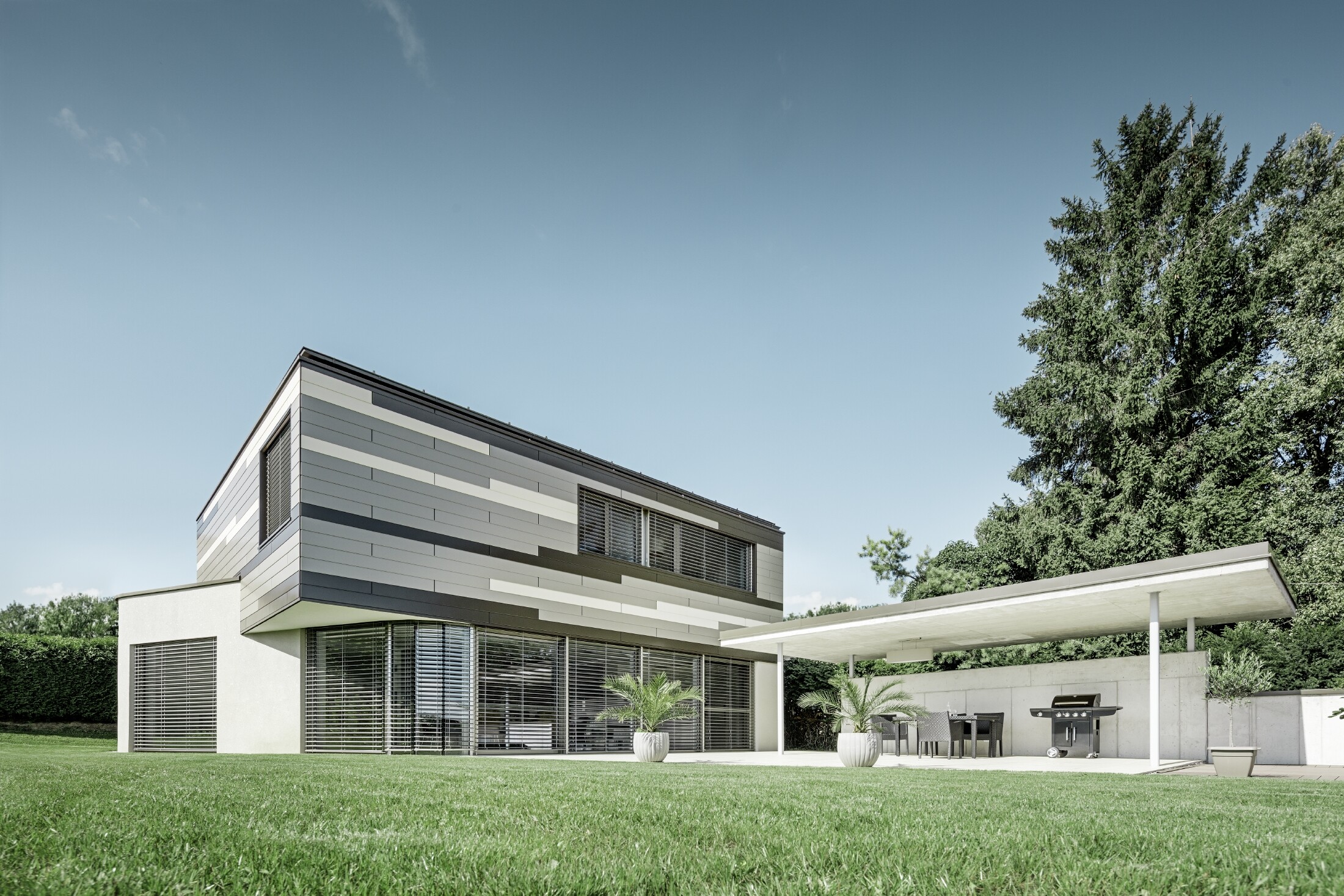 Modernes Einfamilienhaus mit Flachdach und überdachter Terrasse mit einer individuell gestalteten Aluminiumfassade aus Sidings in braun, bronze und elfenbein von PREFA
