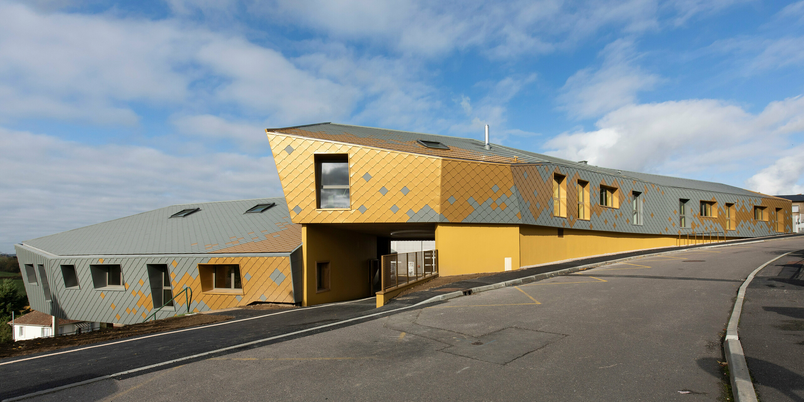 Foto aus der Distanz auf die Grundschule in Pierre-Buffière mit markanten PREFA Dach- und Wandrauten 29 × 29 in  P.10 Hellgrau und Mayagold