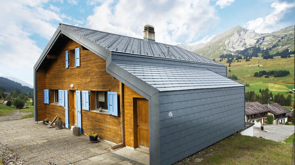Haus in den Bergen der Schweiz mit Holzfassade kombiniert mit der PREFA Dach- und Wandraute in Steingrau
