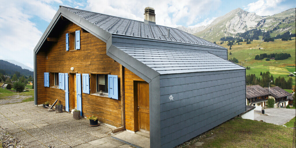 Haus in den Bergen der Schweiz mit Holzfassade kombiniert mit der PREFA Dach- und Wandraute in Steingrau
