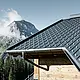 PREFA Dachplatte im alpinen Einsatz - Dachplatte in Anthrazit verlegt auf Hütte in Lech am Arlberg mit Berge im Hintergrund; PREFA Dachrinne in Anthrazit; Holzfassade