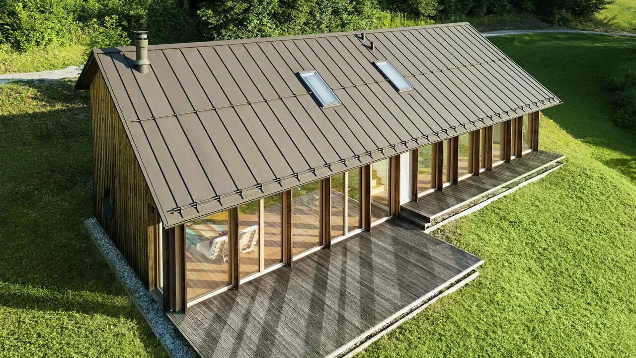 Ein modernes Holzhaus mit großzügiger Glasfassade und einem robusten PREFALZ-Aluminiumdach in der Farbe P.10 Braun – ideal für Hanglagen wie in Vinje. Die hochwertige Dachdeckung garantiert maximale Witterungsbeständigkeit, lange Lebensdauer und eine elegante Optik. Präzise gesetzte Stehfalze und integrierte Dachfenster schaffen ein luftiges und nachhaltiges Wohnkonzept. Die präzise Verarbeitung der Aluminium-Stehfalze wird aus der Vogelperspektive sichtbar.