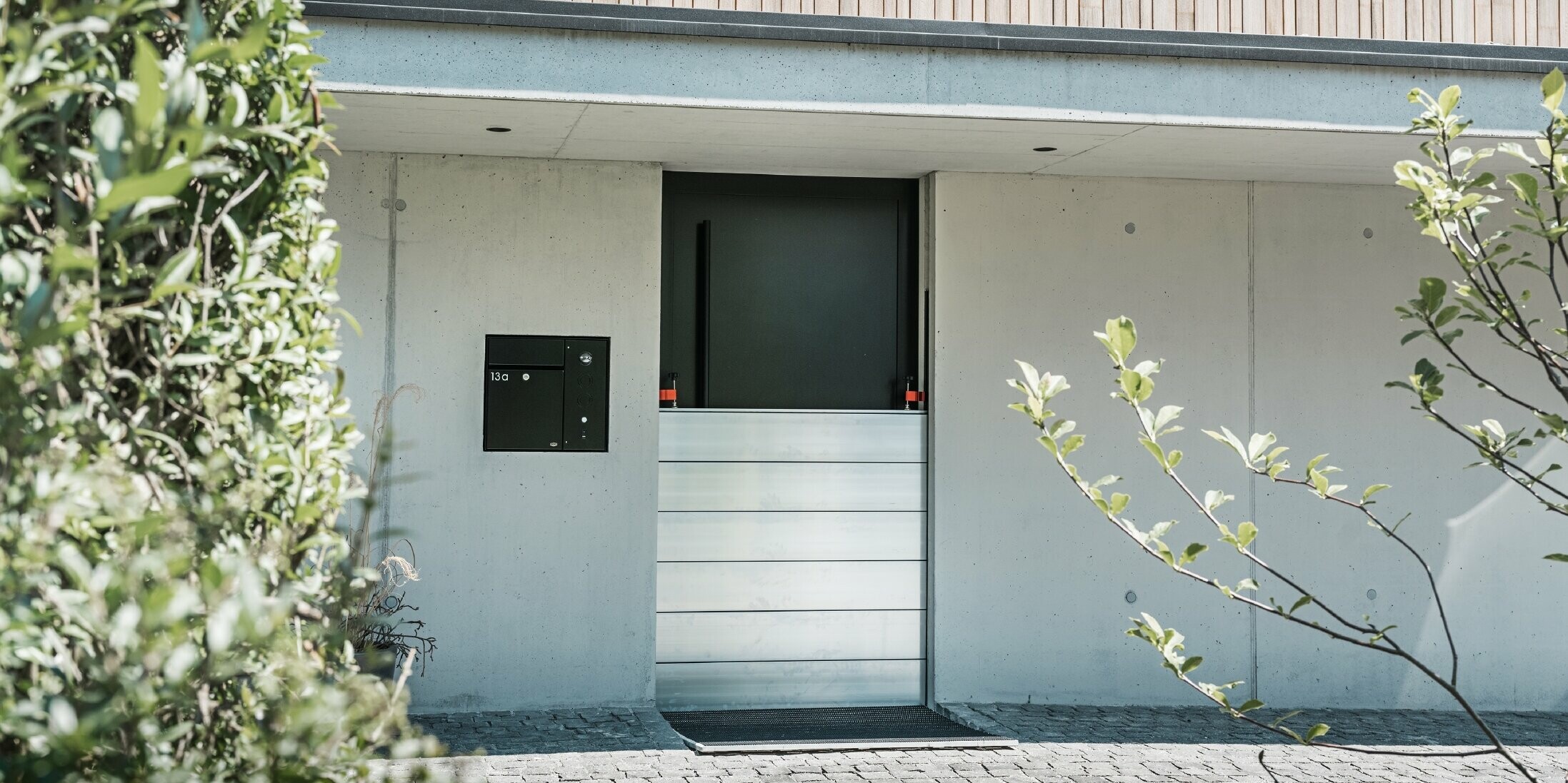 Vor der Eingangstür eines Einfamilienhauses mit Holzfassade wurde der PREFA Hochwasserschutz montiert. Die robusten Dammbalken aus Aluminium garantieren langfristige Sicherheit gegen Hochwasser und Schlamm.