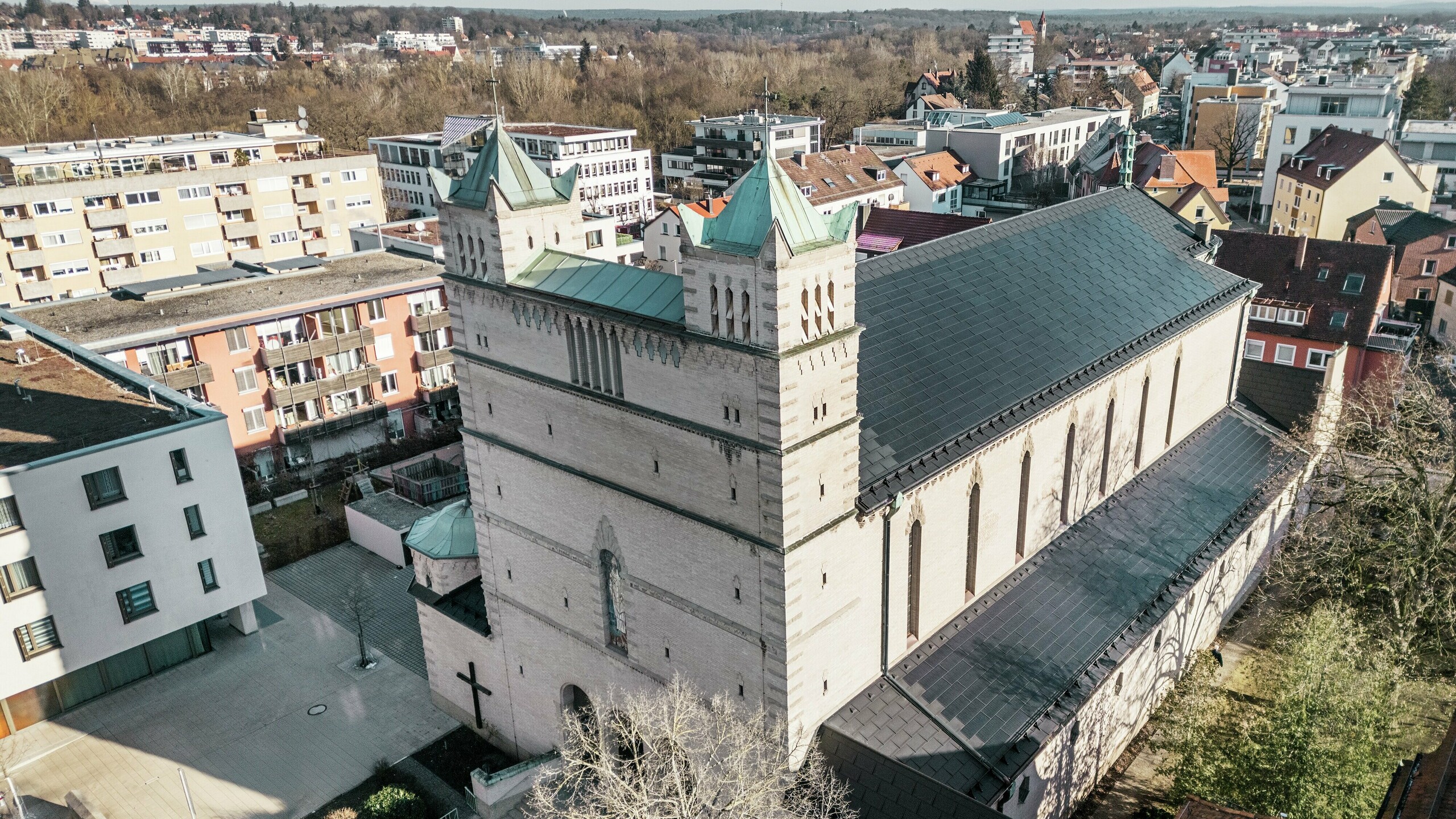 Vorderseite der St. Karl Borromäus Kirche in Nürnberg: Das Bild zeigt das beeindruckende Dach der denkmalgeschützten Kirche, das mit schwarzen PREFA-Solardachplatten gedeckt ist. Die Solarmodule fügen sich harmonisch in die historische Architektur der Kirche ein und stellen gleichzeitig eine moderne Lösung zur nachhaltigen Energiegewinnung dar. Im Hintergrund sind moderne Gebäude und die grünen Hügel Nürnbergs zu sehen, was den gelungenen Übergang zwischen traditioneller Kirchenarchitektur und zeitgemäßer Energieversorgung verdeutlicht. Das Aluminiumdach der Kirche wird durch die stilvolle PREFA Dachplatte R.16 vervollständigt.