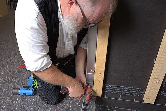 Vogelperspektive auf den PREFA-Techniker Tom Weiß, während er mittels Bohrmaschine ein Loch für einen Niet in die Aluminium-Unterkonstruktion vorbohrt.