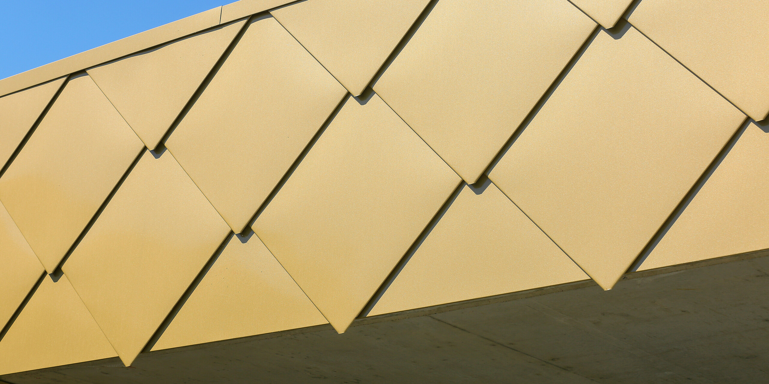Detailaufnahme der glänzenden PREFA Wandrauten 44 × 44 in Sparkling Gold am Kulturzentrum Fessenheim in Frankreich. Die markanten Rauten aus Aluminium lassen das Gebäude in einem auffälligen Gold erstrahlen.