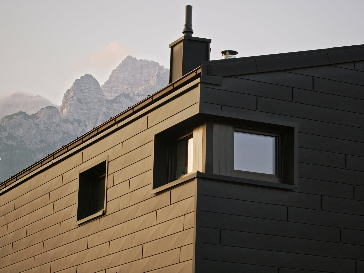 Neugebautes Einfamilienhaus mit schwarzer Siding.X Fassade, im Hintergrund sind die Tiroler Berge zu sehen