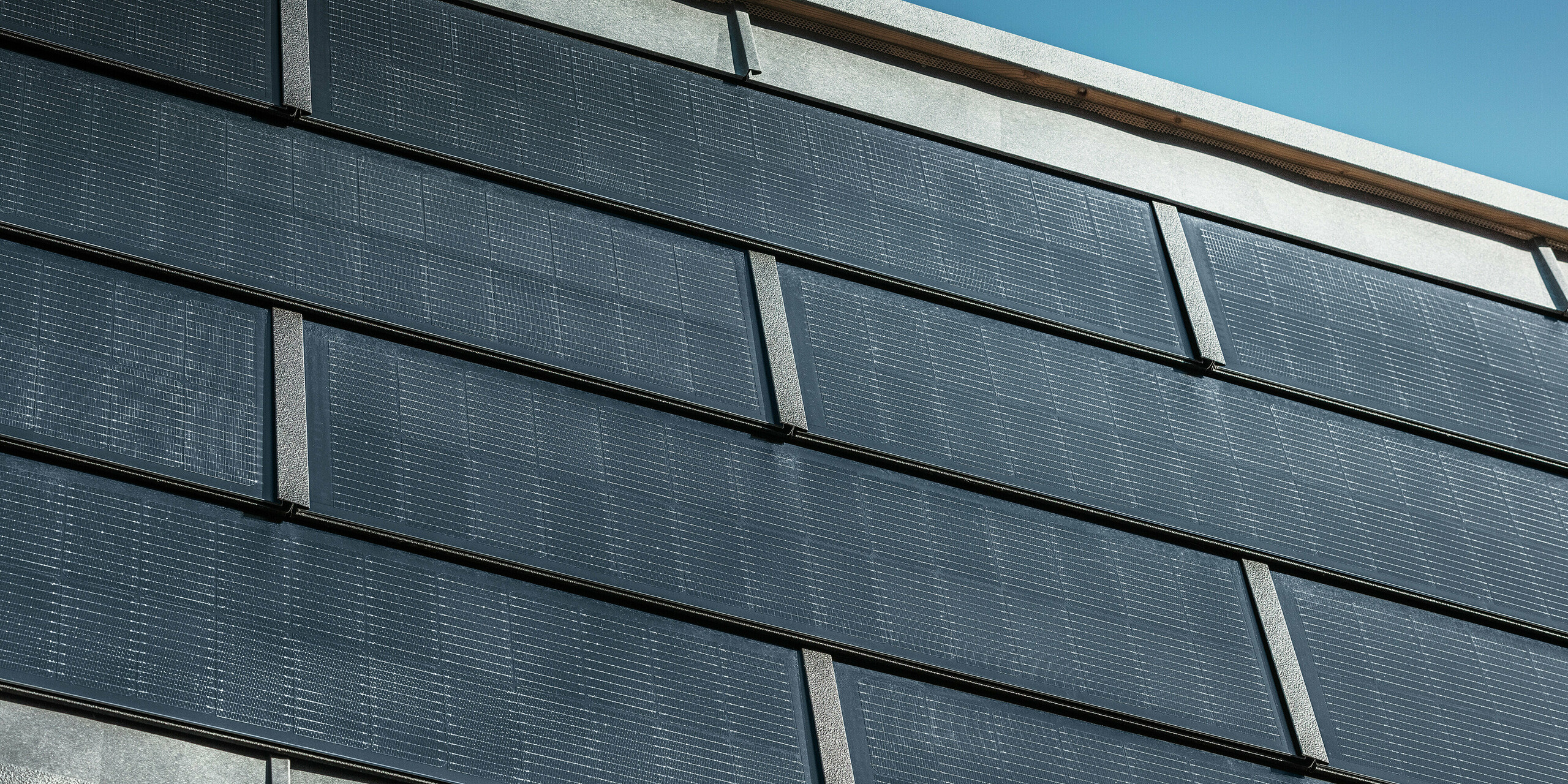 Nahaufnahme der PREFA Solardachplatten mit integrierten Photovoltaikmodulen an der Fassade der Spenglerei RÜMA in Vorarlberg, die modernes Design und nachhaltige Stromerzeugung vereinen.